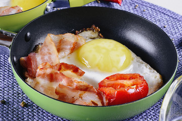 Appetizing and delicious scrambled eggs and bacon in small colored frying pan are on a blue wicker napkin