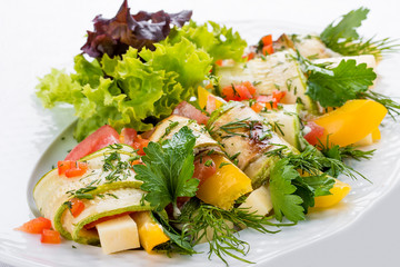 Zucchini rolls with cheese and vegetables on a white plate
