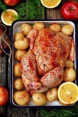 Raw spicy chicken, potatoes and orange slices near apples, cinnamon sticks and cypress branch 