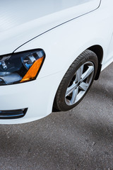 Fototapeta na wymiar cropped image of headlight and wheel of white new car on road