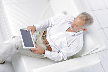 senior businessman looking at digital tablet screen sitting on sofa