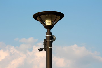 Modern metal black street lamp post with LED lightning and small surveillance camera with motion...