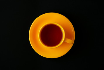 Yellow cup of tea on a black background. View from above. Contrast in the form of a yellow cup of tea in the middle of a black background. Classic tea in a contrasting setting.