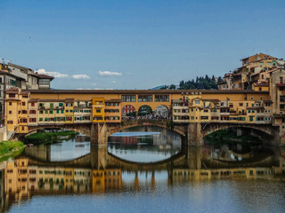 Ponte Vecchio medieval bridge, reflected on Arno river, with sunset light and blue sky background, Florence, Tuscany, Italy