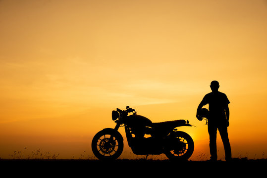 Fototapeta Silhouette of Biker, motorbike parking with sunset background in Thailand. Young Traveller man standing and holding helmet beside motorcycle. Trip and lifestyle of motorbike concept
