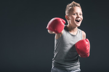 portrait of cheerful boy with red boxing gloves on black backdrop
