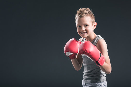 portrait of cheerful boy with red boxing gloves on black backdrop