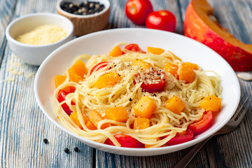 Spaghetti pasta with pumpkin, cherry tomatoes and parmesan cheese in white bowl on vintage wooden background. Selective focus.