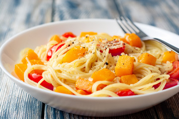 Spaghetti pasta with pumpkin, cherry tomatoes and parmesan cheese in white bowl on vintage wooden background. Selective focus.
