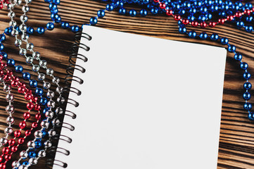 Lot of shiny colorful beads on thread near empty paper notebook with spiral on old wooden table