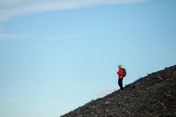 Young sporty girl with backpack admires beautiful view of the ice lake and mountains. Ice lagoon in Iceland