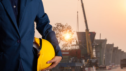 Engineer or worker hold yellow helmet for workers security with theodolite transit equipment at construction site outdoors work.