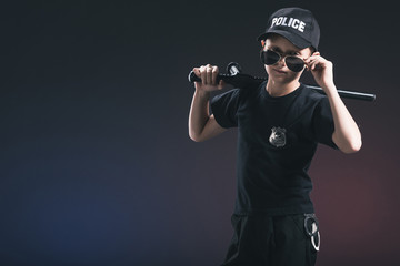 portrait of boy in policeman uniform and sunglasses with truncheon on dark background