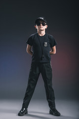 boy in policeman uniform and sunglasses with whistle on dark background