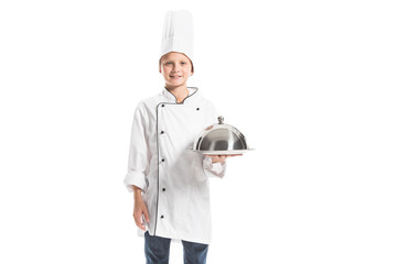 smiling boy in chef uniform and hat holding metal serving tray isolated on white