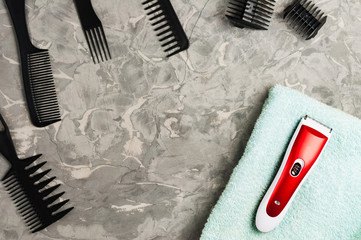 One red and white professional clipper on blue towel and black plastic combs on old gray concrete surface. Top view and copy space
