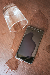 Smartphone wet by accident on wooden table. Glass of water spilled.
