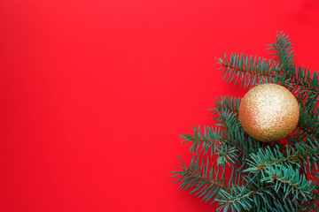 Christmas and New Year background. Golden ball and branches of the Xmas tree on a red background. Copy space.