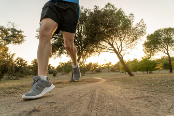 Close up of legs and feet of extreme cross country man running and training on rural track at sunset