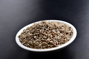 cumin jeera seeds , indian spices, ceramic bowl on black background