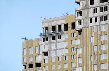 Process of mounting insulation on apartment building facade in new modern urban house over blue sky with clouds closeup