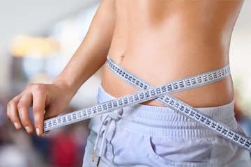 Slim young woman measuring her thin waist