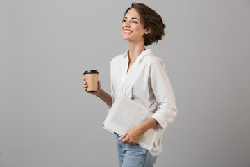 Happy young woman posing isolated over grey background drinking coffee.