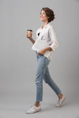 Happy young woman posing isolated over grey background drinking coffee.