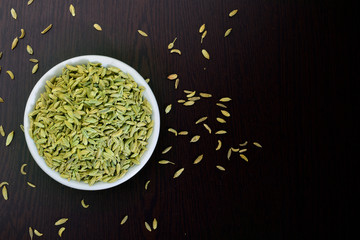 fennel seeds in ceremic bowl on dark wooden background , top view