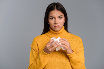 Ill woman standing isolated over grey wall background holding napkin.