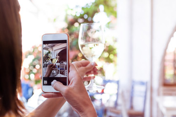 Woman taking photo of white wine on her smartphone in restaurant. Bali island.