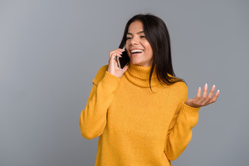 Happy woman posing isolated over grey wall background talking by mobile phone.