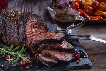 Appetizing roast beef with sauce and spices on a wooden table next to sauce and grilled vegetables