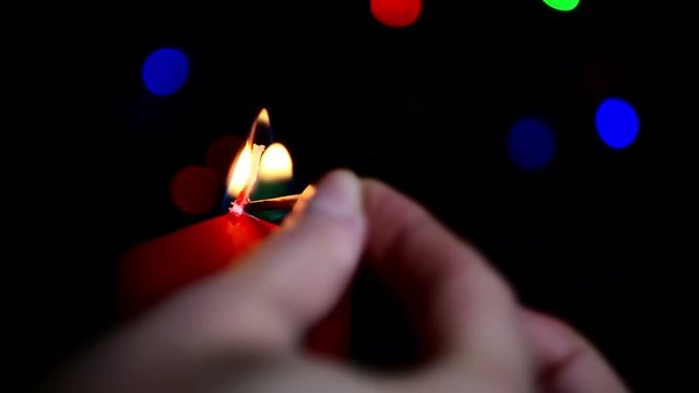 The girl lights a large red candle on the background of boke. Close-up of a burning candle.