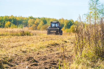 Autumn field with a red tractor that mows dry grass, Russia