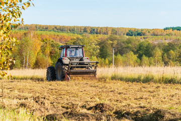 Autumn field with a red tractor that mows dry grass, Russia