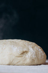Ball of raw dough sprinkled with flour on rustic wooden counter