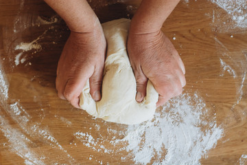 Hands kneading raw dough on wooden table