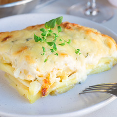 Piece of cheesy scalloped potatoes or potato gratin on a plate, holiday theme, square format