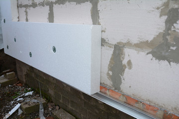 Builder installing anchors in house wall for rigid insulation foam.