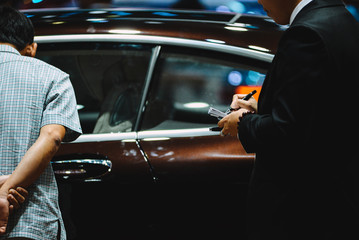 An unidentified man in a black vest holding a notebook was walking across a black modern car. Handsome elegant man in suit, businessman or salesman, stretches his hand to conclude a business.