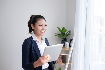 Strong, confident, Asian business woman standing in an office building hallway, holding tablet computer