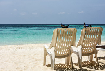 Beach easy armchairs by the blue turquoise sea with local tourist boats in the distant background. Tranquil scene of Thailand tourism in the south.