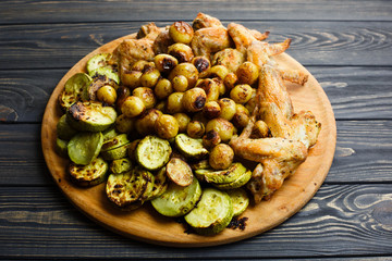 Grilled vegetables and chicken wings on the wooden plate