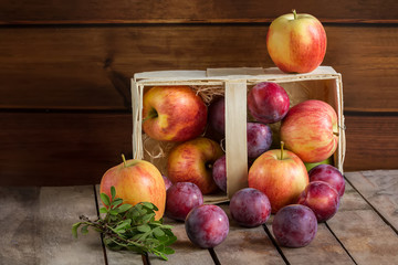 Gifts of autumn: apples and plums in a basket on a wooden background, autumn composition, harvest