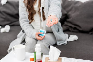 cropped shot of sick woman in warm clothes holding pill in hand