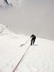 mountain climber rappelling off s steep snowy mountain peak in the Swiss Alps above Zermatt