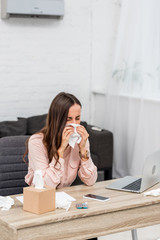 ill young businesswoman blowing nose with paper napkin at workplace