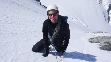 Fototapeta na wymiar mountain climber high up on a steep north face in snow and ice looks up and smiles