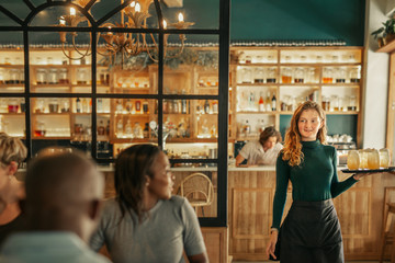 Smiling waitress bringing drinks to people sitting in a bar